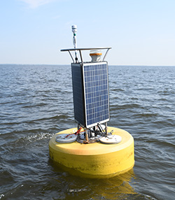 A yellow-hulled buoy, topped with solar panels and sensors, floats in water